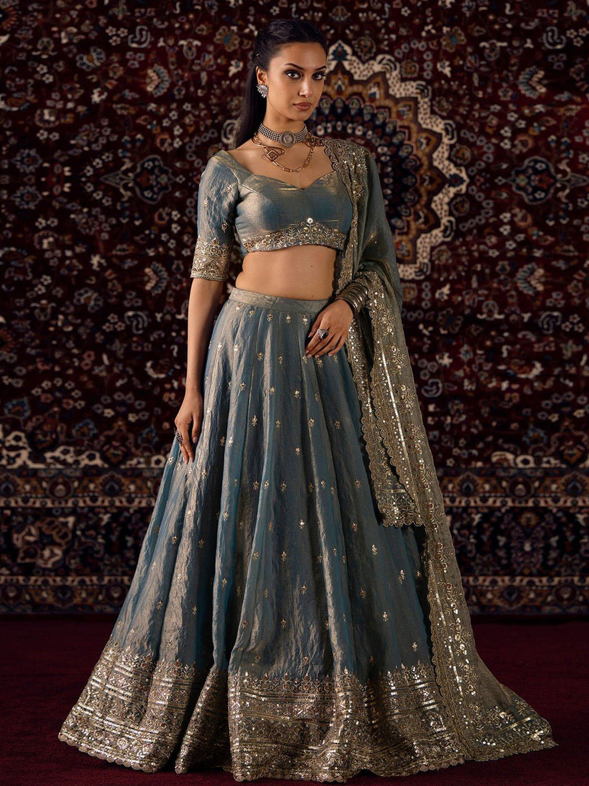 Buy a designer silk lehenga choli featuring dusty blue colour, golden shading, rich Zari embroidery, sequin work and a customizable blouse.